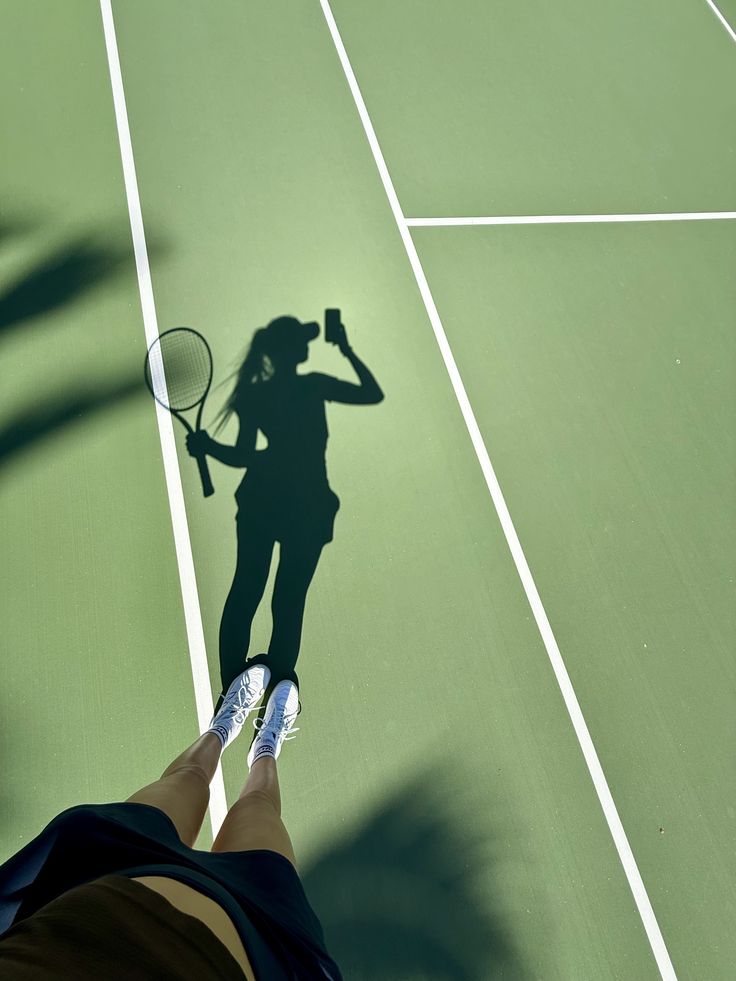 Shadow selfie on a green court with racket in hand